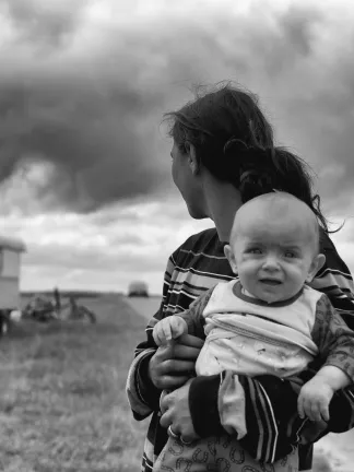 A mother holding a baby looking back at her trailer