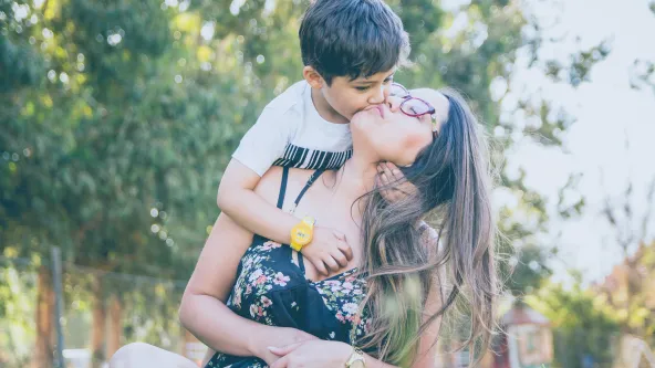 A mother sitting and a child hugging her from behind