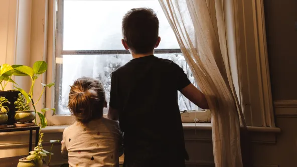 Two small children look out a window of a home
